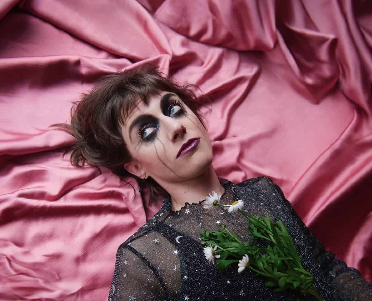 Jane Mumford mit Blumen auf schwarzem Kleid auf rosa Satinbett.